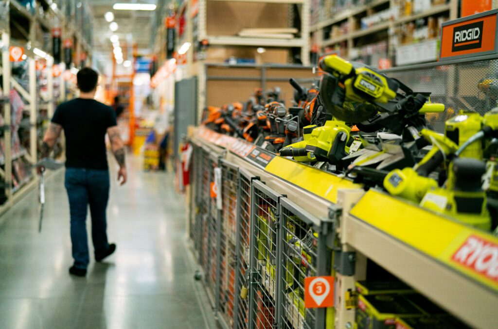 Eine Person geht durch einen Gang eines Baumarkts, dessen Regale mit verschiedenen Elektrowerkzeugen bestückt sind, darunter Marken wie Ryobi und Ridgid. Dies veranschaulicht, wie die digitale Transformation den B2B-Vertrieb in Unternehmen wie der Wego Systembaustoffe GmbH beeinflusst.